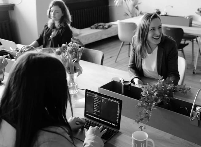 Three young women at work in an office, programming and smiling.